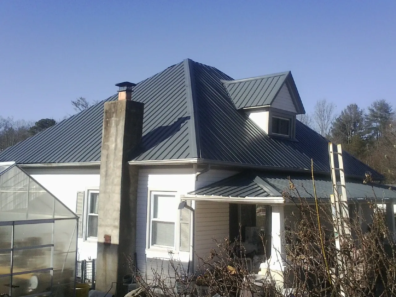 Dark blue standing seam metal roof on a white farmhouse with dormer — Slate & Tile Roof Repair by Roofing Brothers in Anahuac