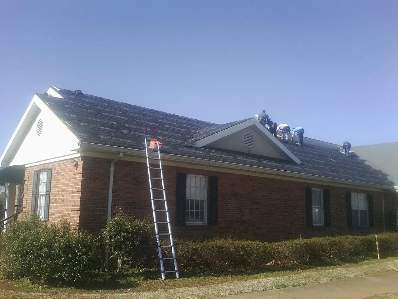 Crew tearing shingles off a brick ranch roof with a ladder set — Emergency Roof Repair work by our crew in Anahuac