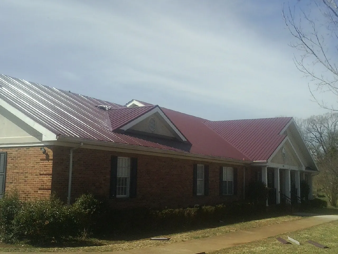 Red metal roof with gabled entries on a long brick building, from a Hail Damage Roof Repair job in Anahuac