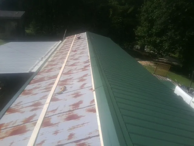 Old rusted panels beside newly installed green metal roofing — Wind Damage Roof Repair by Roofing Brothers in Anahuac