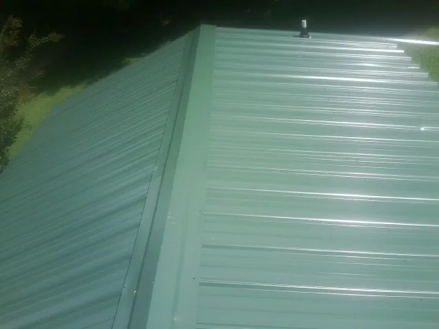 New green metal panels meeting at the ridge of a roof — Flat Roof Repair work by our crew in Anahuac
