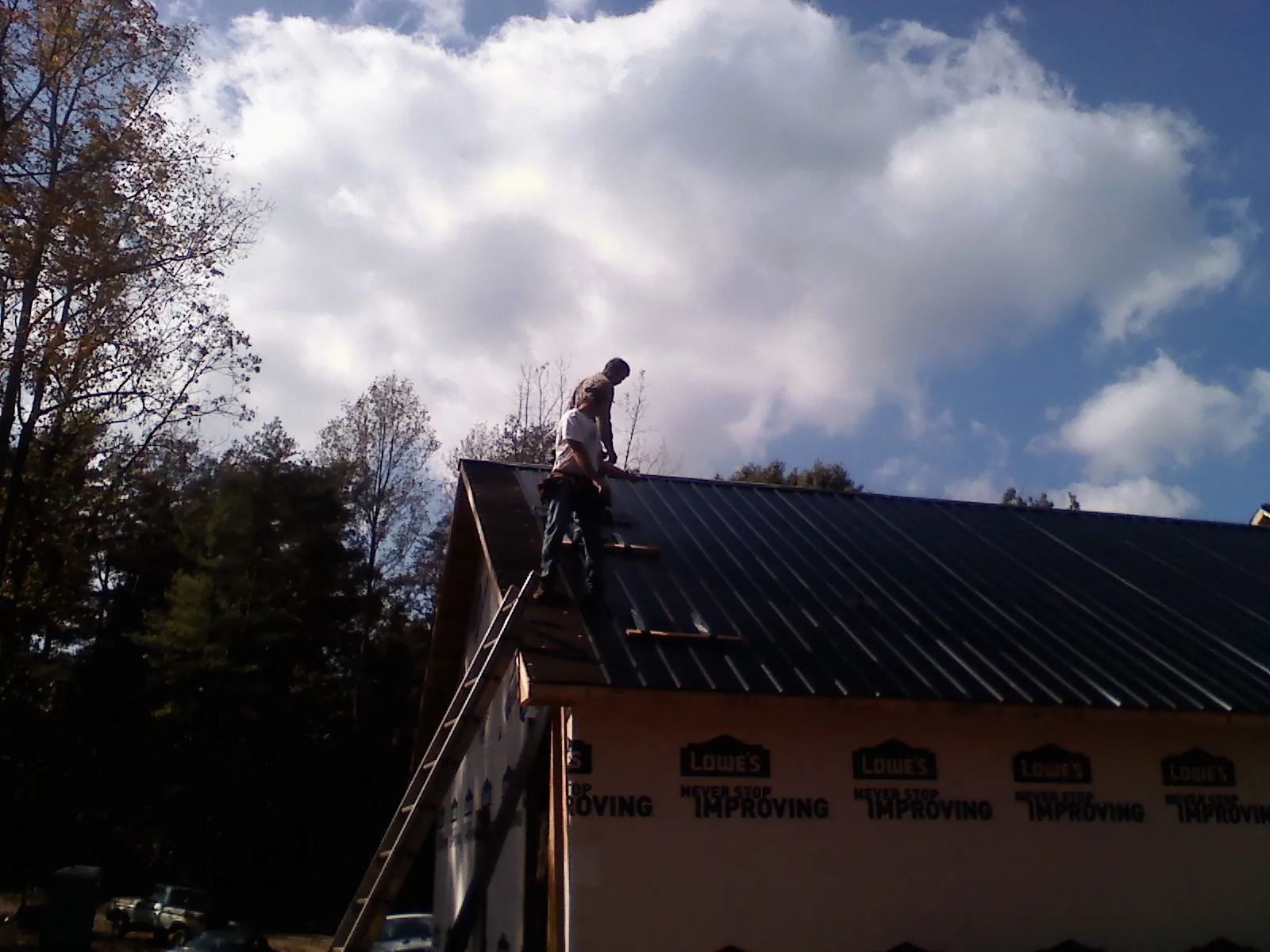 Roofer fastening dark metal panels high against a cloudy sky, from a Roof Inspection job in Anahuac