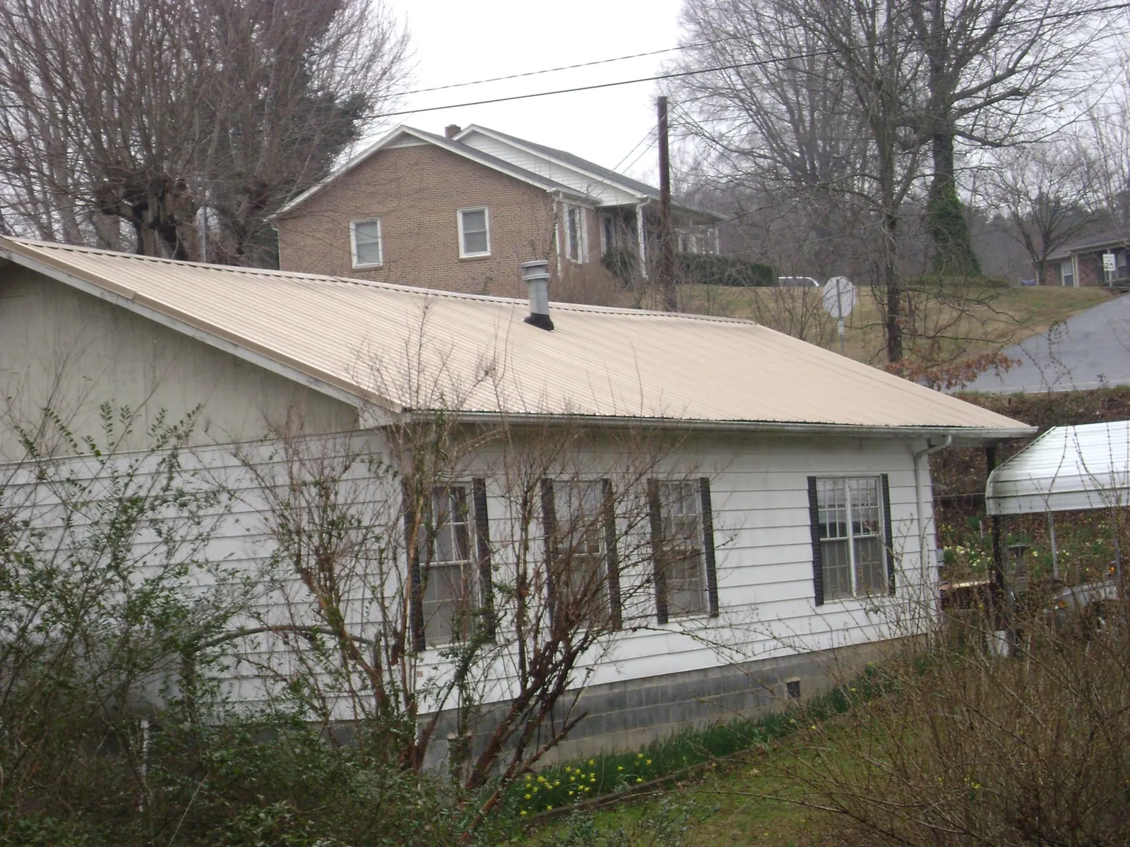 Tan metal roof on a white sided house set into a hillside — Commercial Roofing by Roofing Brothers in Anahuac