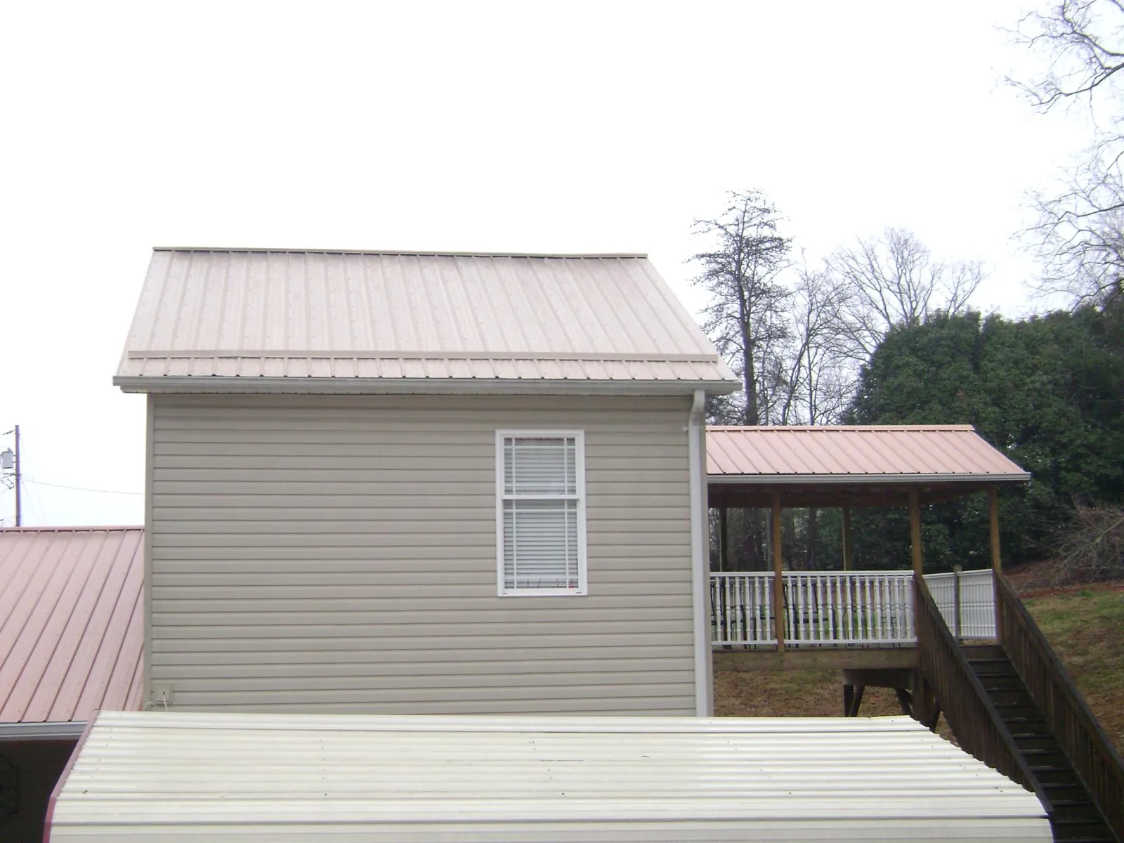 Tan metal roofs on a two story addition and attached porch, from a Roof Replacement job in Anahuac